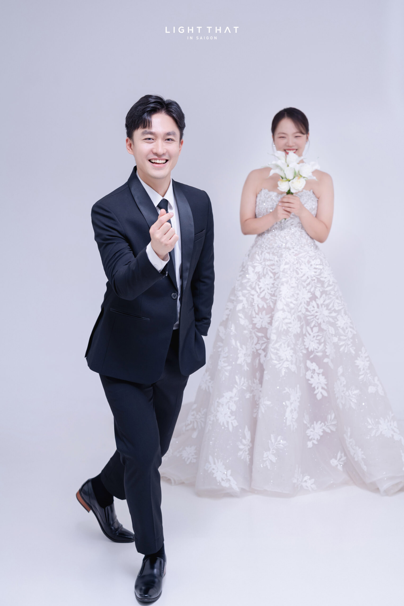 Cặp đôi tạo dáng tựa lưng, nắm tay nhẹ nhàng trong không gian phông trơn đen