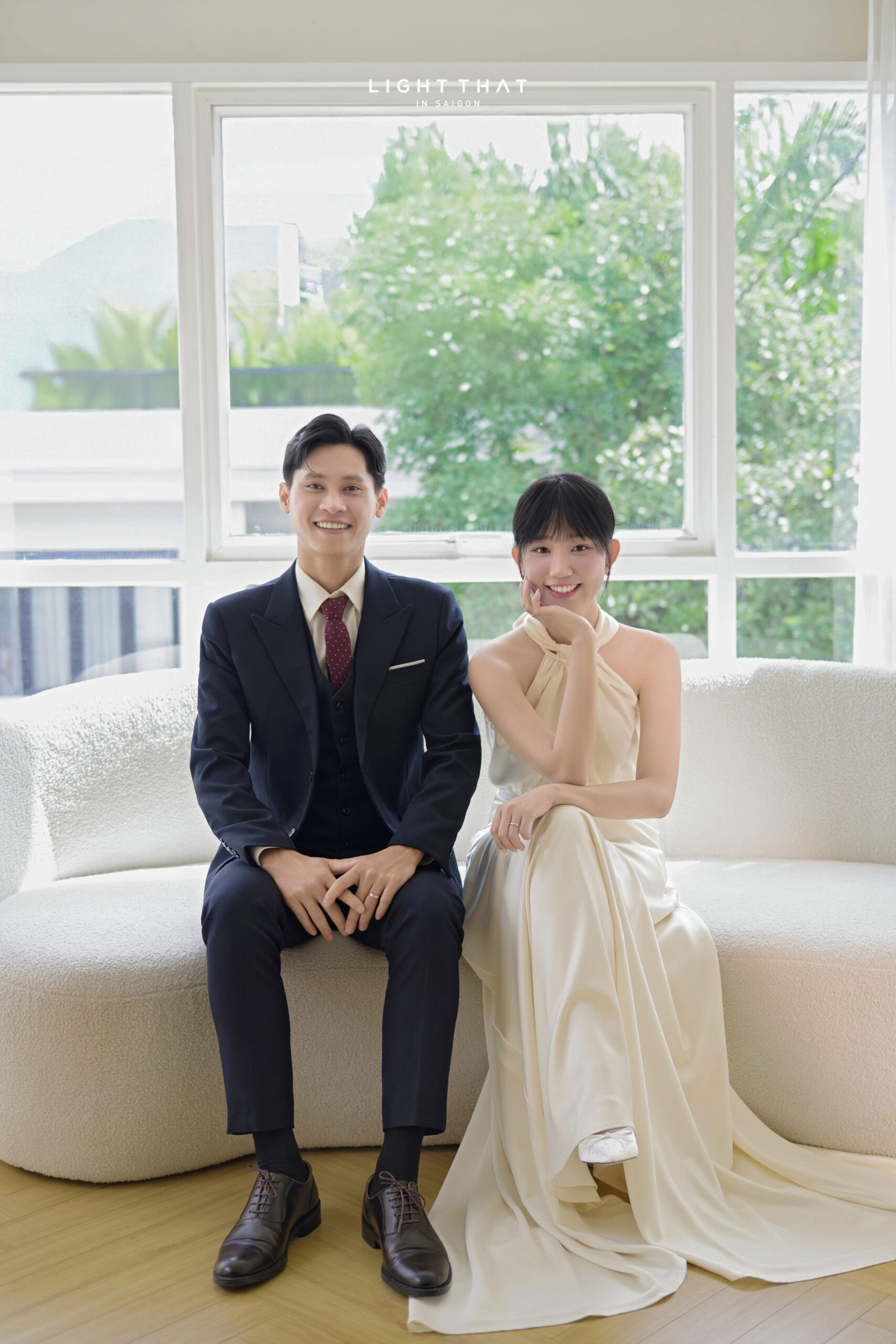 Cặp đôi ngồi trên ghế, tạo dáng thanh lịch, cô dâu cầm hoa nhìn nhẹ về máy