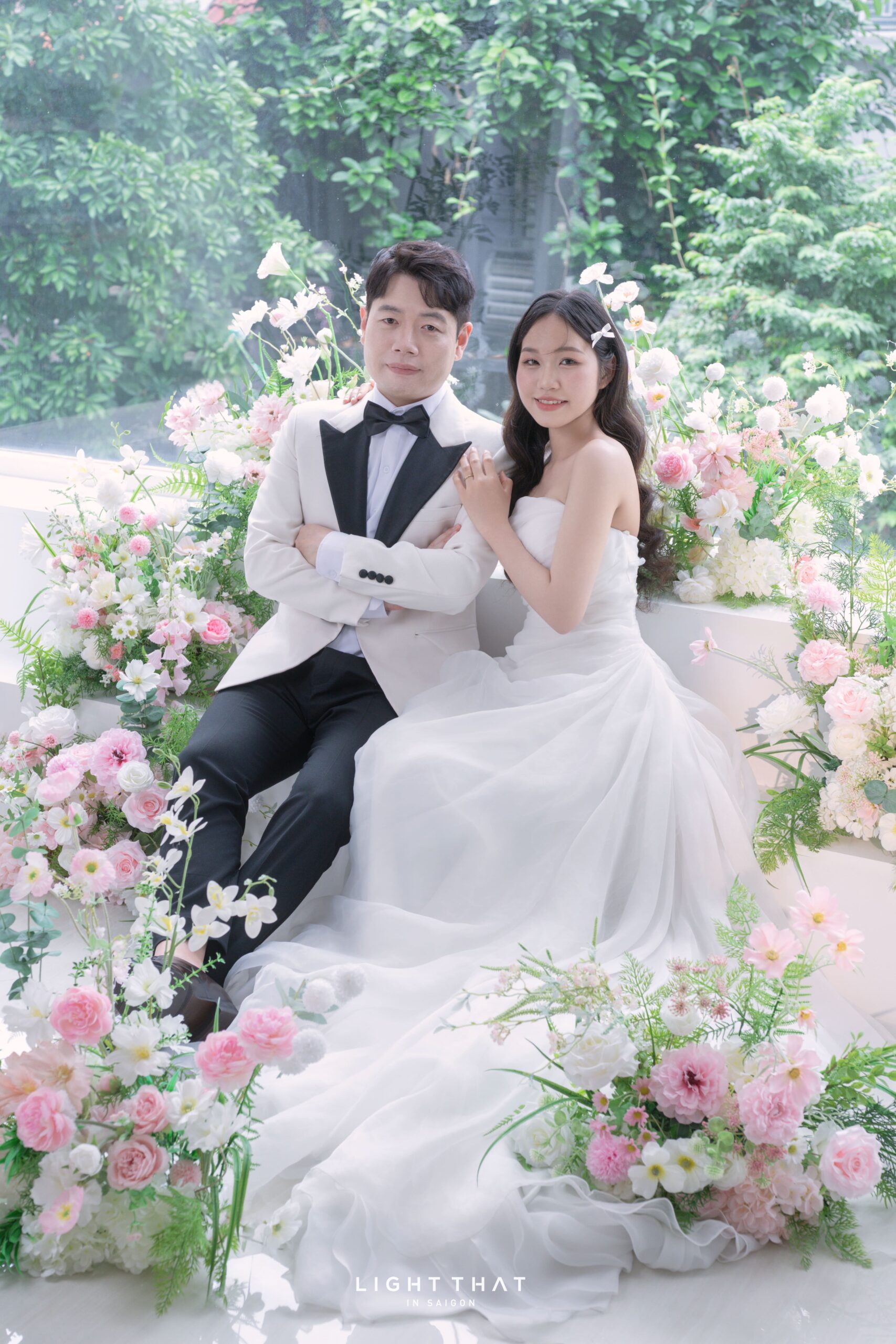 Cô dâu chú rể ngồi giữa vườn hoa, ánh sáng tự nhiên, biểu cảm dịu dàng